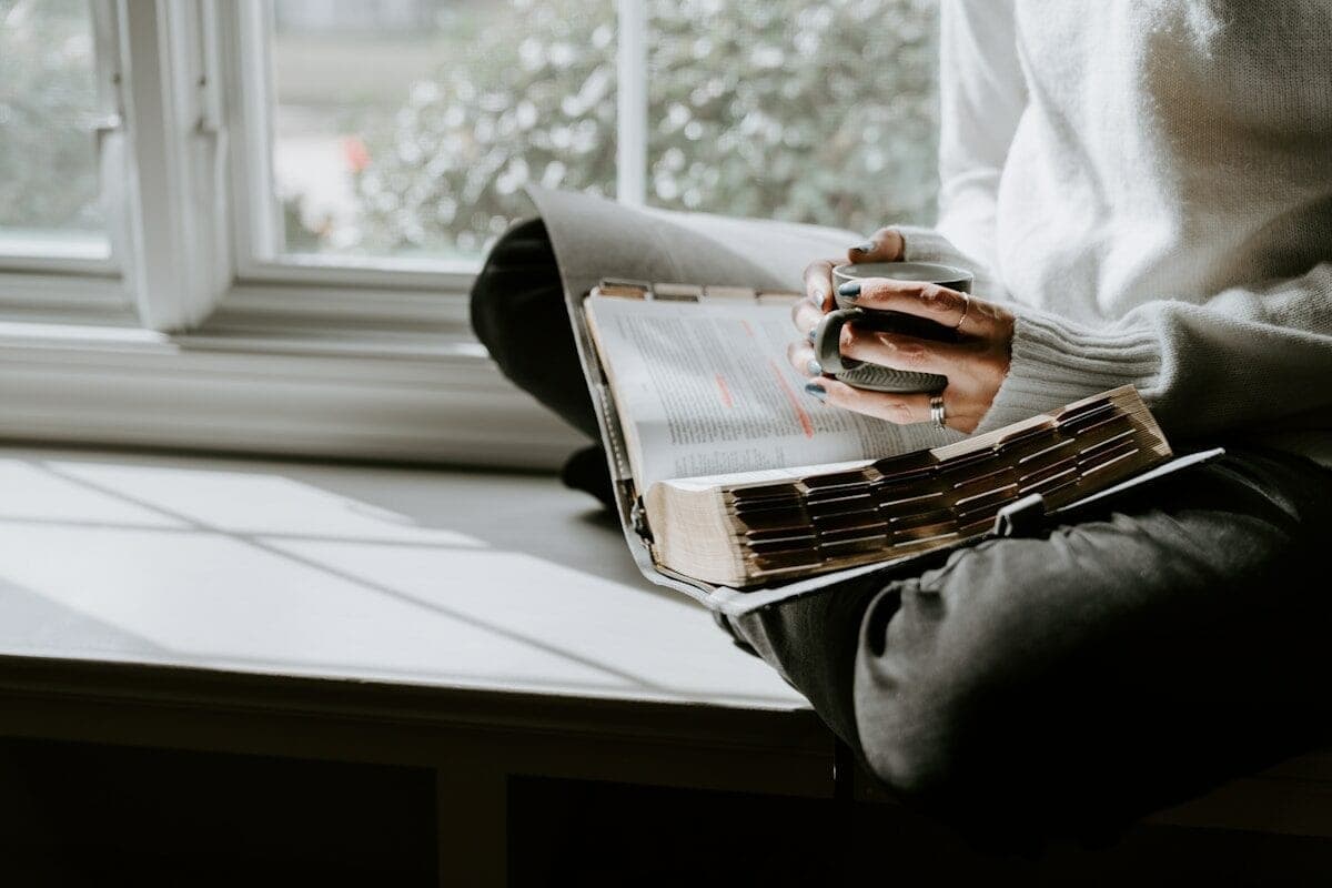 A person sitting on a window sill reading a book