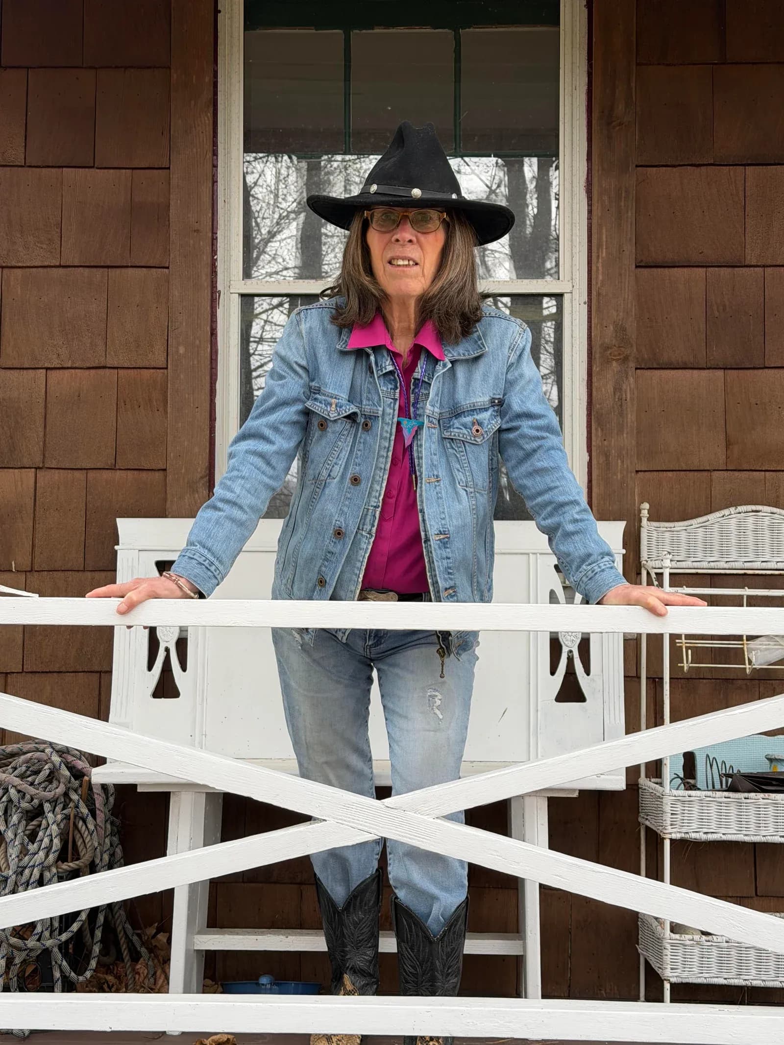 Christa Jan Ryan, author of The Compliant Cowgirl, on her porch in a cowboy hat and denim jacket