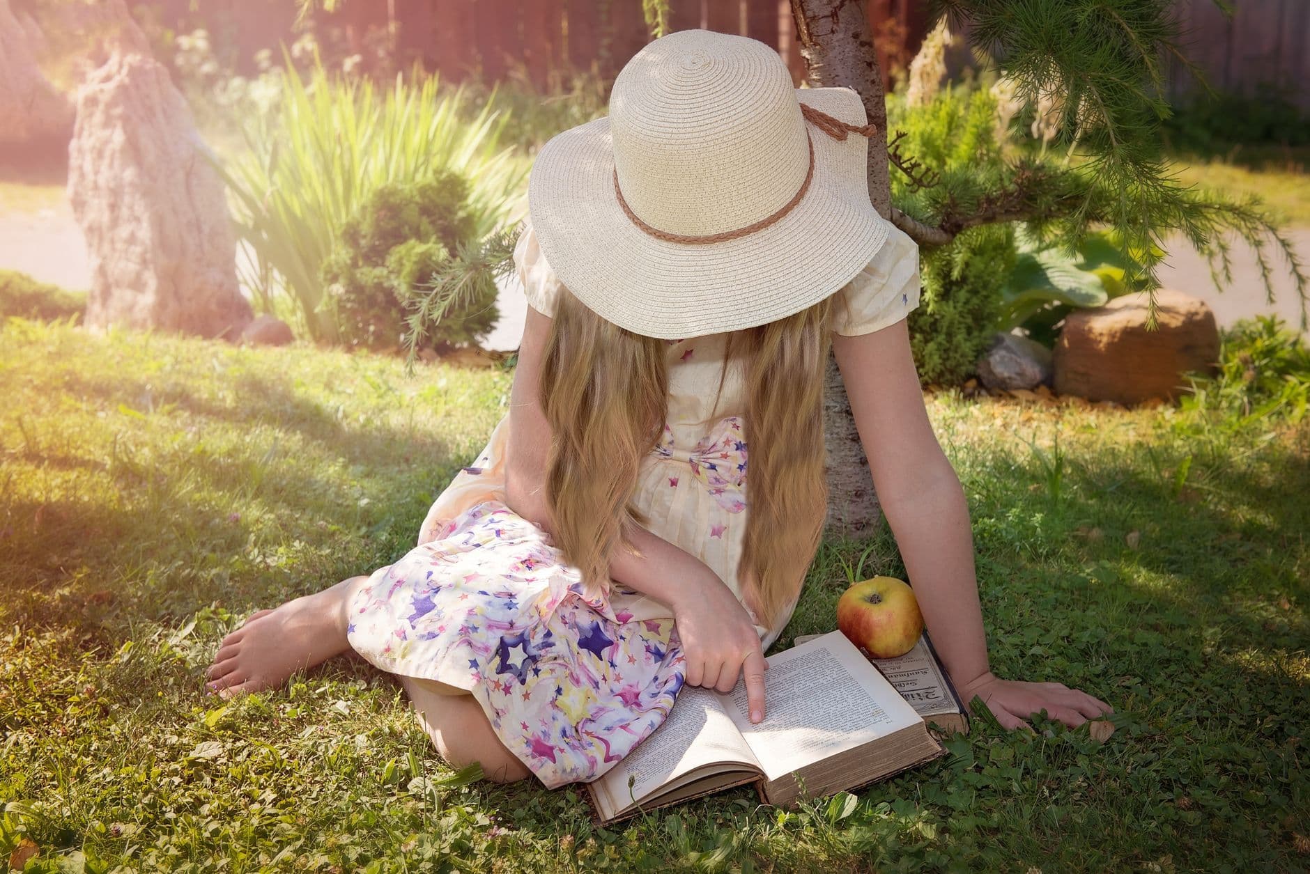 A young girl reads a book under a tree during a sunny summer day, exuding peace and relaxation.